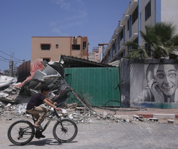 A boy bikes in front of buildings destroyed by conflict in Gaza.