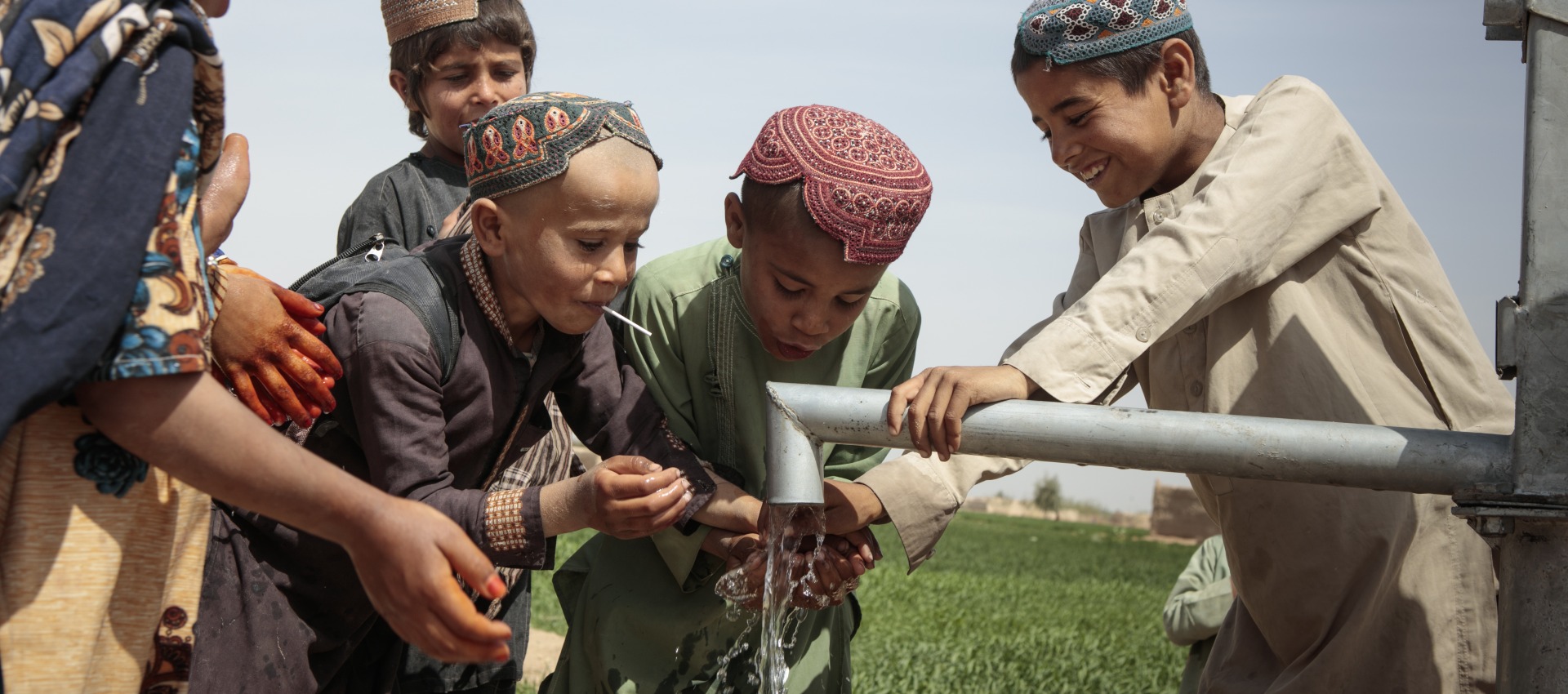 School-age children play with water from a pump.