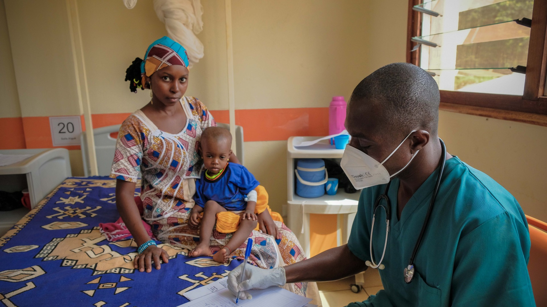 Un agent de santé portant un masque avec une mère et son enfant à l'hôpital pédiatrique de Bangui, en République centrafricaine.