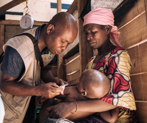 A health worker checks the nutrition status of a young boy as his mother holds him.