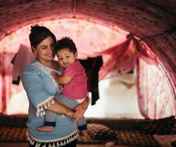 A displaced woman holds her daughter in a tent