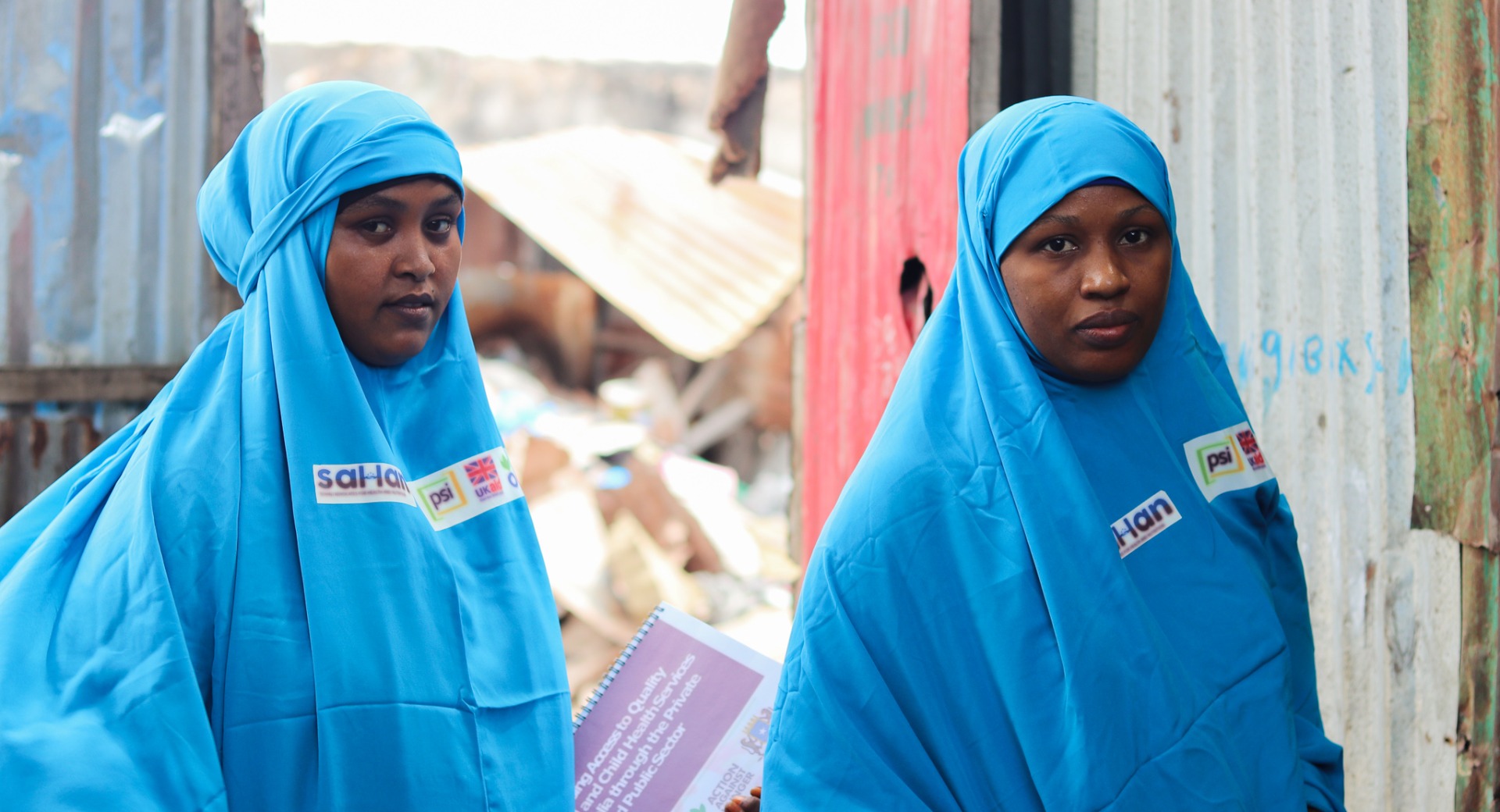 Two Female Community Influencers, Fardosa (left) and Amina (right), pose before they head into a home to meet with a mother.