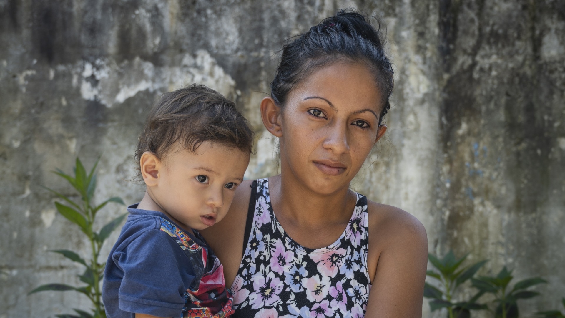 A woman stands, holding a young boy in her arms.