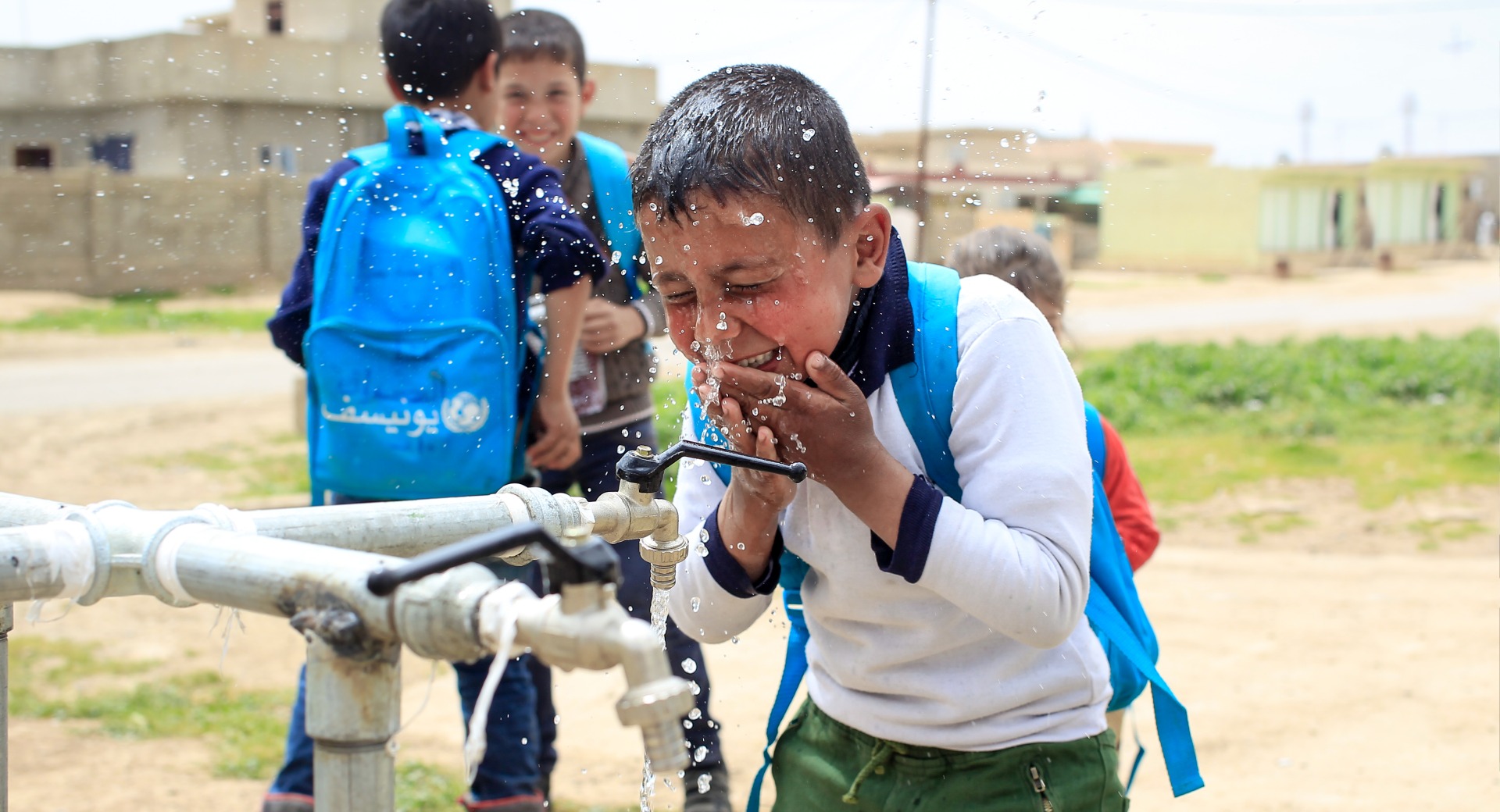 A boy splashes water on his face at a tap installed by Action Against Hunger.