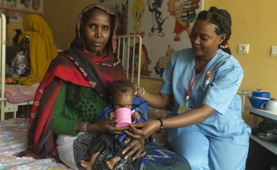 At the Stabilization Center at Yabelo General Hospital in Ethiopia, Nurse Ware helps severely malnourished Dabo drink therapeutic milk as treatment for Dabo's malnutrition.