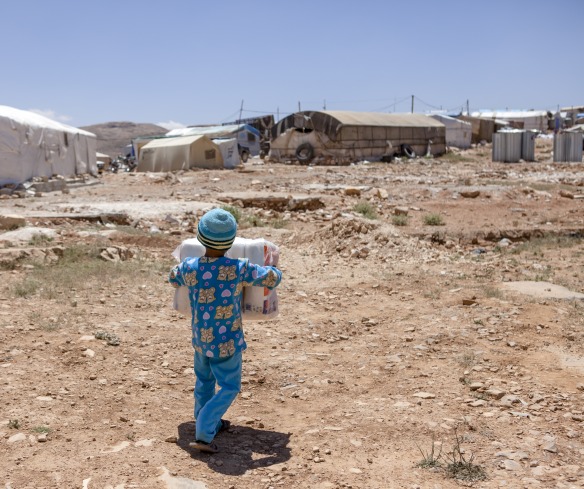 Ala, 7, carries back diapers for his little brother provided by Action Against Hunger in s settlement in Aarsal, Lebanon, near the Syrian border.