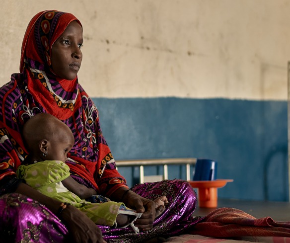 In a health center in Chad, a woman sits on a bed with her malnourished child.