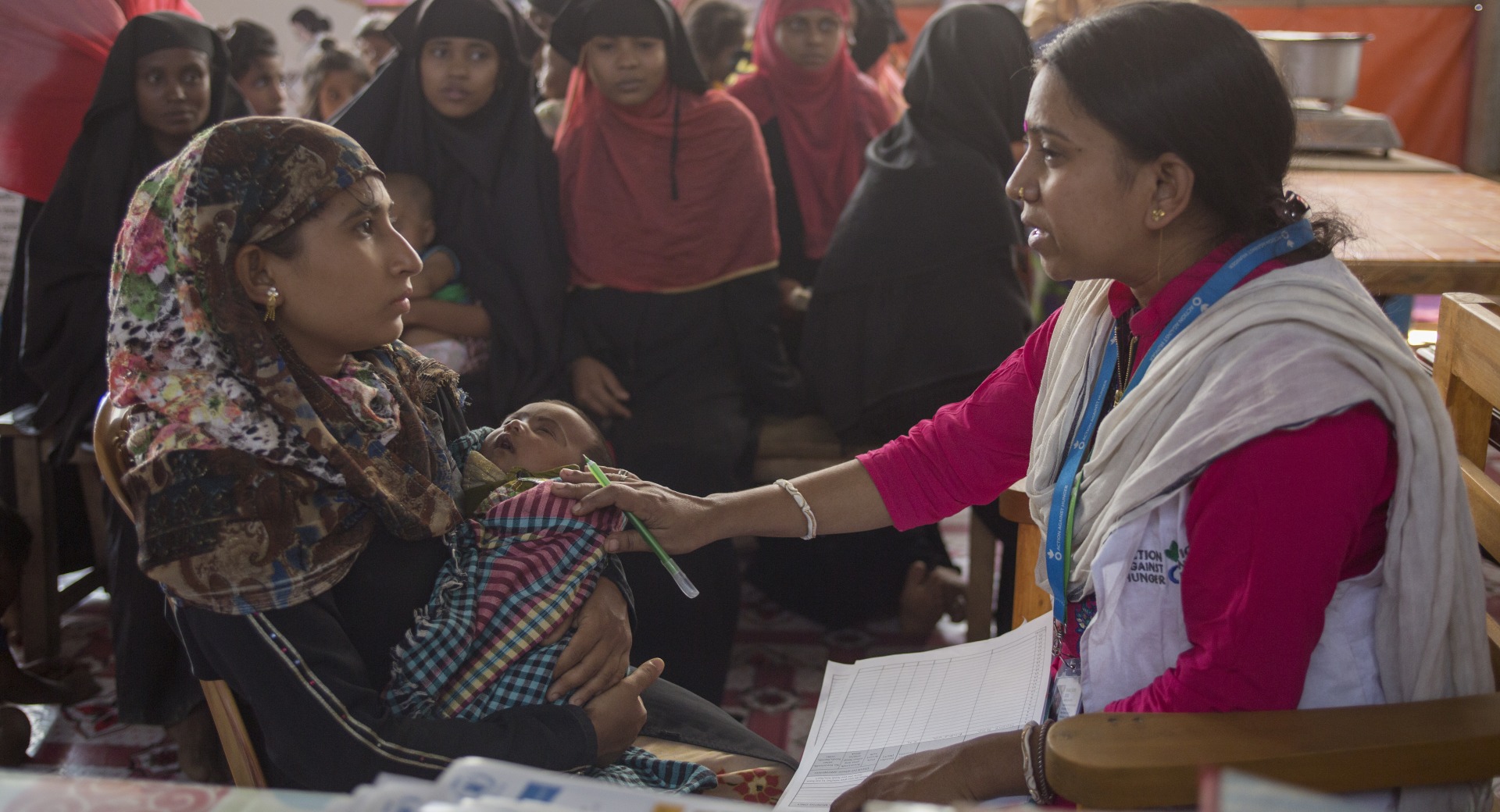 Shaki Rani Bose, responsable de l'éducation à la santé, s'entretient avec une jeune mère, Hosne Ara, et son bébé, entourée de femmes Rohinga qui attendent patiemment d'être examinées dans une clinique d'Action contre la faim pour les femmes enceintes et les mères allaitantes.