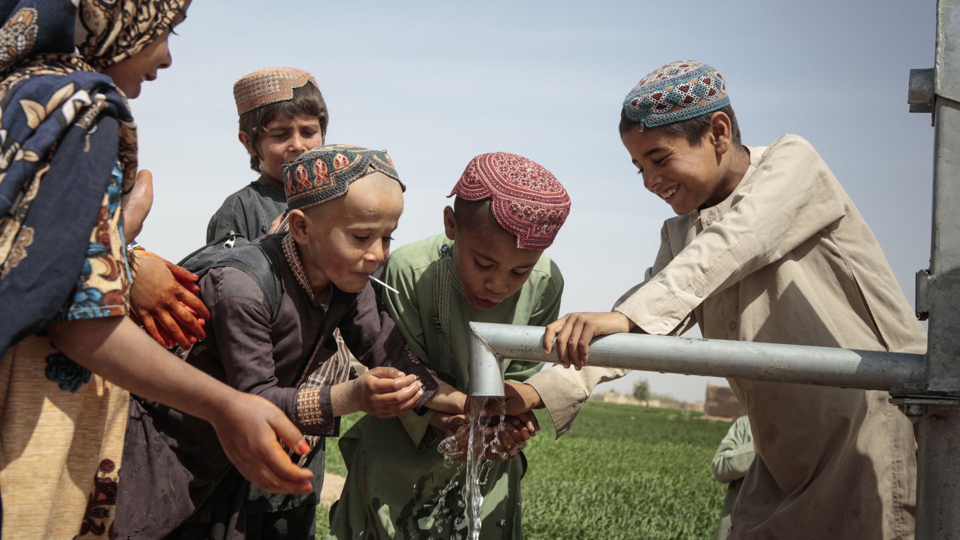 School-age children play with water from a pump.