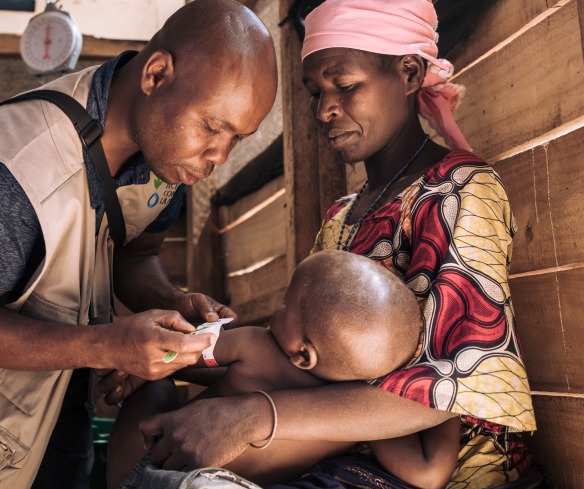 A health worker checks the nutrition status of a young boy as his mother holds him.