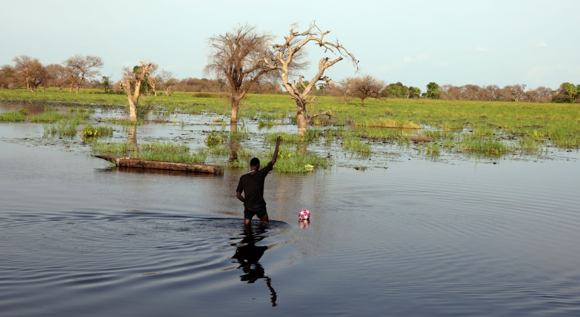 In the final game of a tournament, the ball is kicked so hard, it ends up off the pitch and in the floodwaters. A kind spectator wades in to get it back.