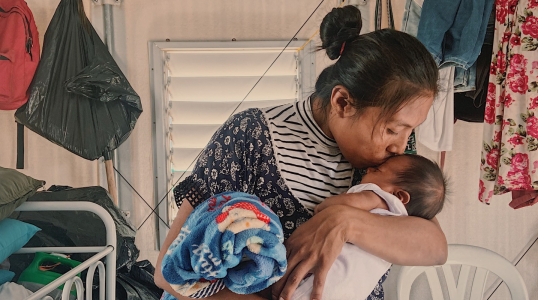 A mother kisses her baby. Her family was displaced by conflict and now receives cash support from Action Against Hunger.